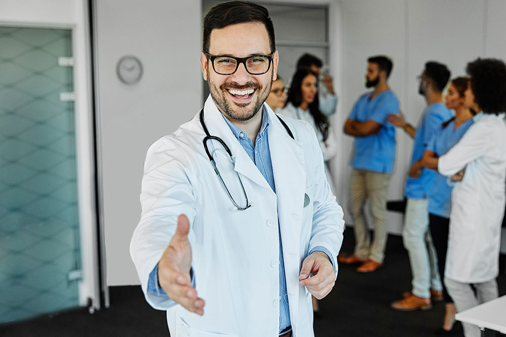 Porträt eines jungen, selbstbewussten und freundlichen Arztes, der vor einer Gruppe von Ärzten und Krankenschwestern die Hand reicht. Teamwork, Kooperation und Gesundheitskonzept